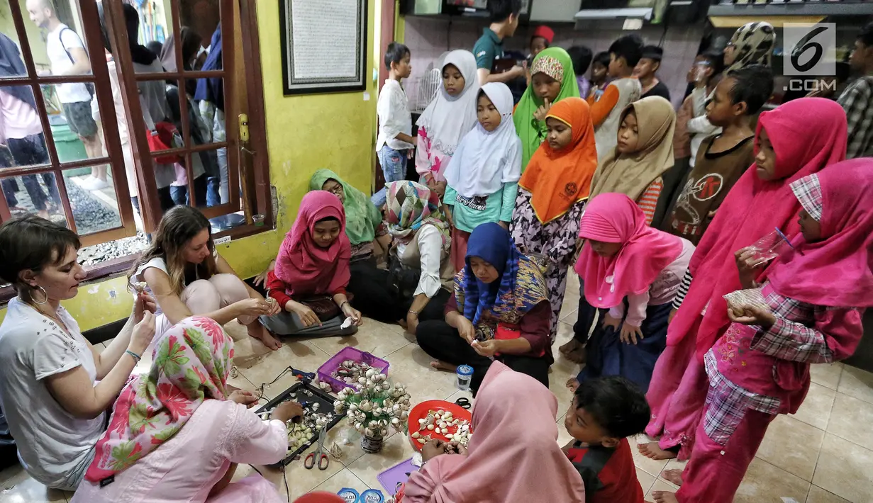 Anak-anak melihat dua warga negara asing (WNA) membuat membuat kreasi daur ulang dari daun bawang di Rumah Amalia, Ciledug, Kota Tangerang, Sabtu (3/3). Kegiatan kreativitas ini dibantu ibu-ibu sekitar. (Liputan6.com/Fery Pradolo)