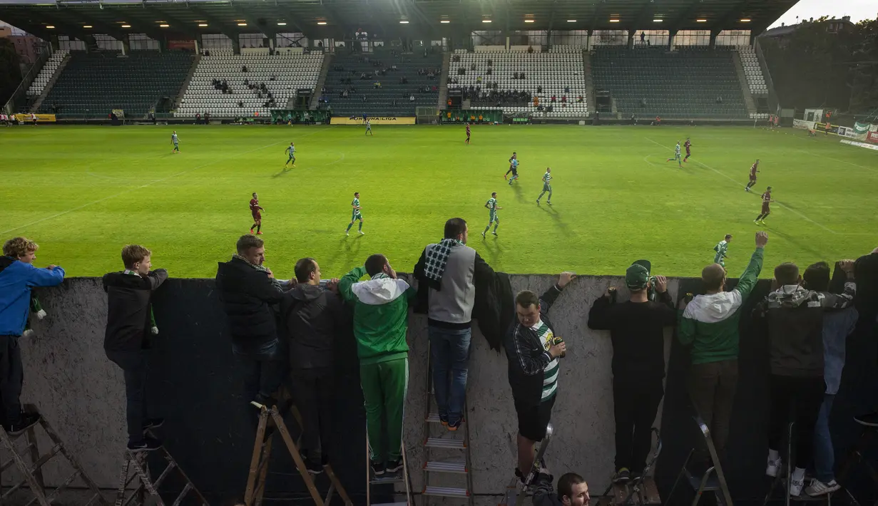 Suporter Bohemians 1905 menyaksikan pertandingan Czech First League alias Liga Fortuna melawan Sparta Praha dari balik tembok di Praha, Rep. Ceko pada 6 Juni 2020. Dengan menggunakan tangga, mereka menonton laga yang tertutup di tengah pembatasan virus corona Covid-19. (Michal Cizek/AFP)