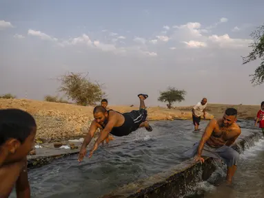 Warga Palestina meluncur di kanal air yang digunakan untuk irigasi untuk mendinginkan tubuh saat suhu udara mencapai 44 derajat Celcius di kota Jericho, Tepi Barat (1/9/2020). (AFP Photo/Ahmad Gharabli)