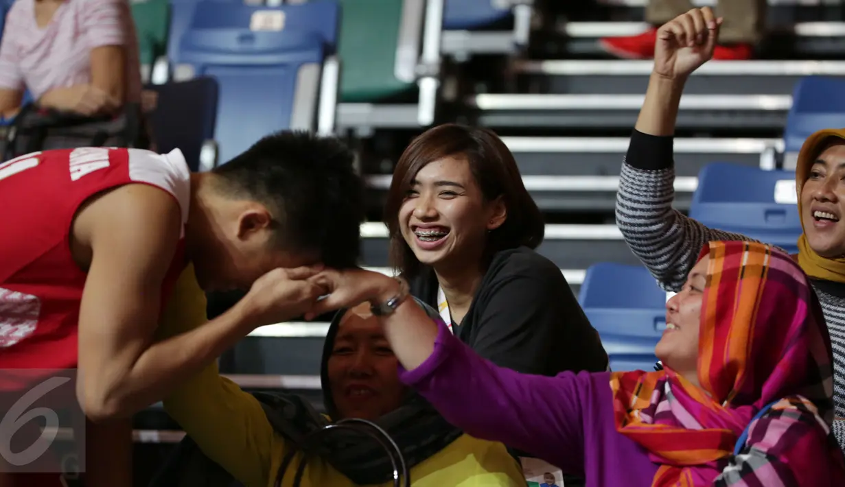 Pevoli Yolla Yuliana (tengah) tersenyum menyaksikan pebasket Indonesia, Andakara Prastawa Dhyaksa mencium tangan salah satu kerabatnya usai berlaga di semifinal SEA Games ke-28 di OCBC Arena Singapore, Minggu (14/6/2015). (Liputan6.com/Helmi Fithriansyah)