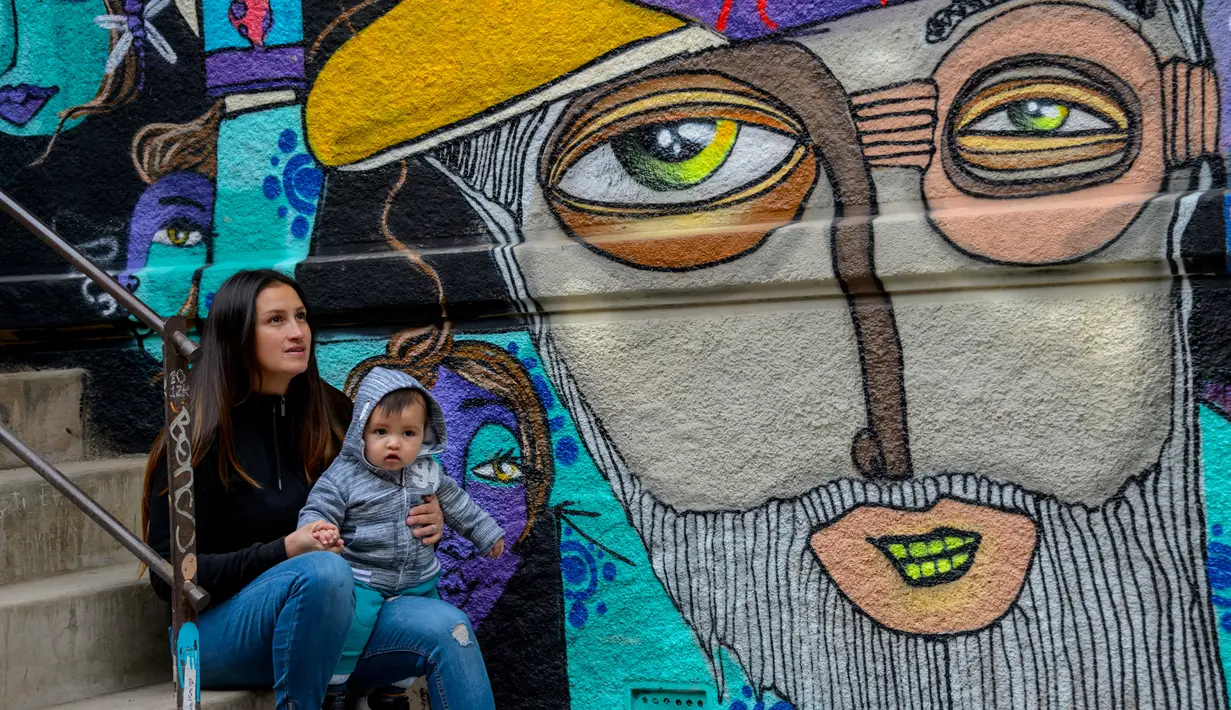 Seniman Cynthia Aguilera berpose bersama putranya di sebelah mural buatannya di Valparaiso, Chile, 9 April 2019. Selama beberapa tahun terakhir, tembok di sepanjang Elias Street di Valparaiso diubah menjadi kanvas raksasa tempat seniman jalanan memamerkan keterampilan mereka. (Martin BERNETTI/AFP)