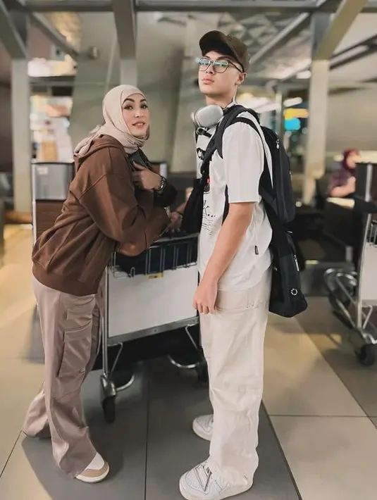Saat berangkat, outfit airport Angelina Sondakh mengenakan hoodie coklat dipadukan celana berkantong depan dan pashmina coklat muda. [@angelinasondakh09]