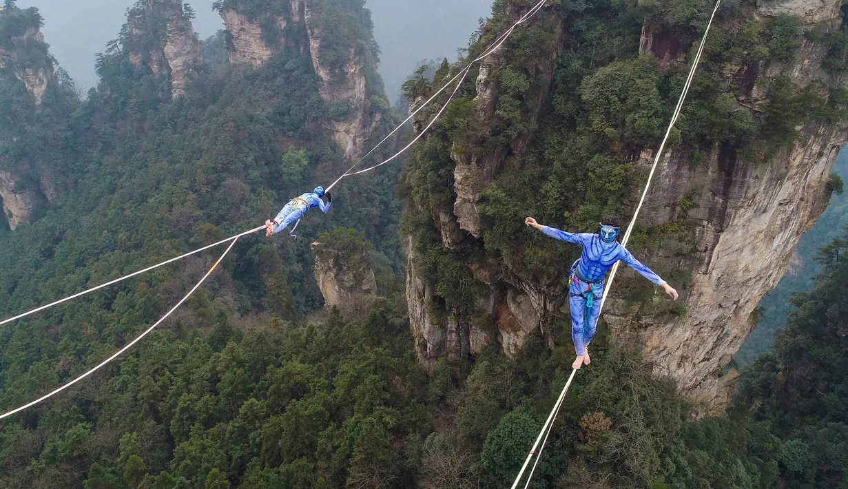 Dua kontestan berpakaian karakter Avatar berpacu sepanjang slackline di Pegunungan Huangshizhai di Zhangjiajie, Hunan, China, Minggu (23/12). Lanskap pegunungan ini menjadi rujukan film Avatar yang ternyata ada di Bumi. (STR/AFP) (STR/AFP)