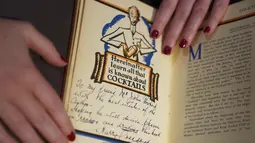 Seorang asisten galeri menunjukkan Savoy Cocktail Book, Harry Craddock (1876 - 1963), diperkirakan antara £1.500 - £2000, selama kunjungan foto untuk sorotan dari Penjualan Minggu Klasik yang akan datang, di Christies, London (3/12/2021). (Kirsty O'Connor/PA via AP)