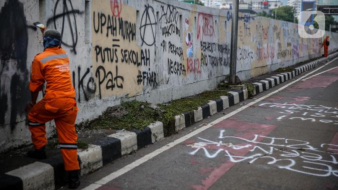 Petugas PPSU membersihkan coretan yang mengotori pembatas jalan pascaunjuk rasa di kawasan DPR/MPR, Jakarta, Jumat (17/7/2020). Coretan tersebut dilakukan oleh massa yang menolak RUU Omnibus Law Cipta Lapangan Kerja di depan Gedung DPR pada Kamis (16/7) kemarin. (Liputan6.com/Faizal Fanani)