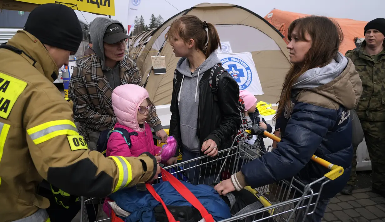 Petugas damkar Polandia membantu pengungsi Ukraina membawa barang-barang di perbatasan Medyka, Rabu (30/3/2022). Badan pengungsi PBB mengatakan kini lebih dari 4 juta orang telah meninggalkan Ukraina, tonggak baru dalam krisis pengungsi terbesar di Eropa sejak Dunia Perang II. (AP/Sergei Grits)