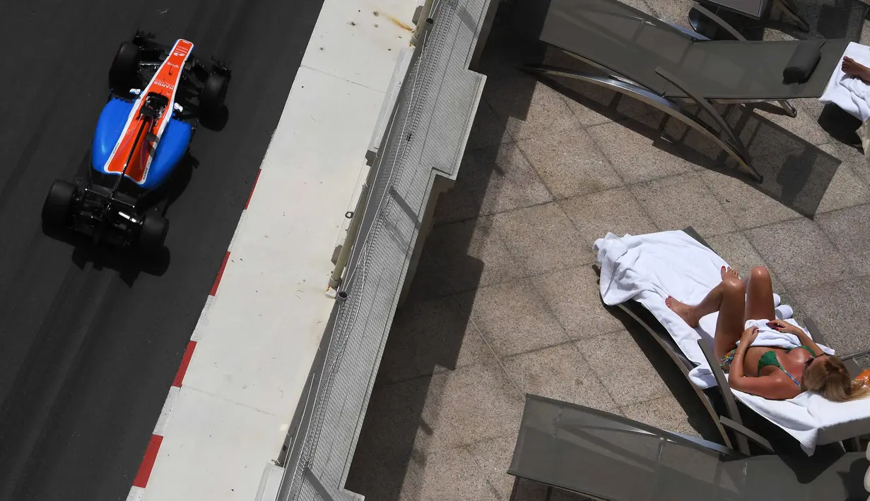 Pebalap Manor Racing, Pascal Wehrlein, melintas di dekat seorang turis yang sedang berjemur sambil menyaksikan latihan bebas F1 GP Monako di sirkuit jalan raya Monako. (AFP/Pascal Guyot)