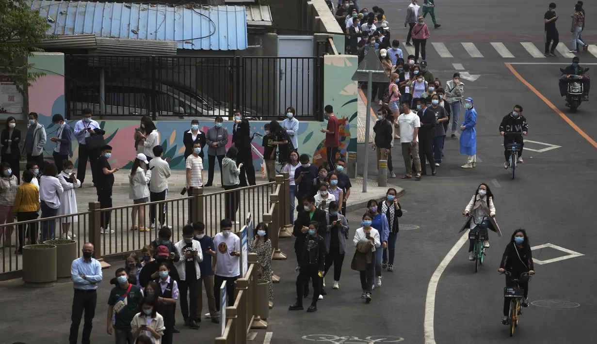 <p>Pengendara sepeda melewati warga dan pekerja kantor yang mengantre di jalan untuk pengujian virus corona massal di dekat kompleks perumahan dan perkantoran komersial di kawasan pusat bisnis, Beijing, Senin (25/4/2022). (AP Photo/Andy Wong)</p>
