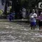 Warga melintasi genangan air yang merendam jalan di kawasan Kampung Makasar, Jakarta Timur, Senin (7/7/2025). (Liputan6.com/Herman Zakharia)