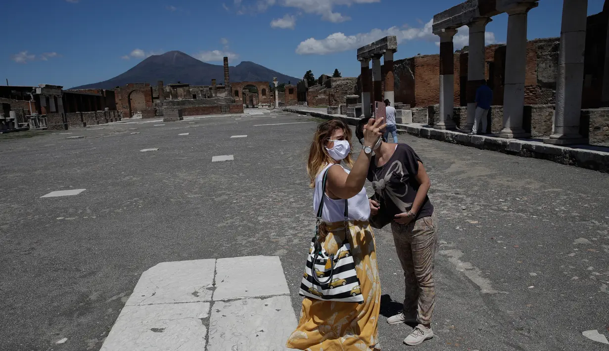 Dua perempuan berswafoto saat mengunjungi situs arkeologi Pompeii usai kebijakan lockdown selama dua bulan untuk mengendalikan penyebaran Covid-19 di Italia, Selasa (26/5/2020). Salah satu situs arkeologi paling terkenal di dunia ini dibuka kembali untuk umum pada 26 Mei. (AP/Alessandra Tarantino)