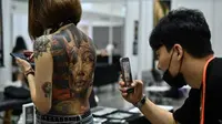 Seorang laki-laki mengambil gambar badan wanita yang dipenuhi tato pada saat acara International Malaysia Tattoo Expo di Kuala Lumpur, Malaysia.(AFP/Mohd Rasfan)