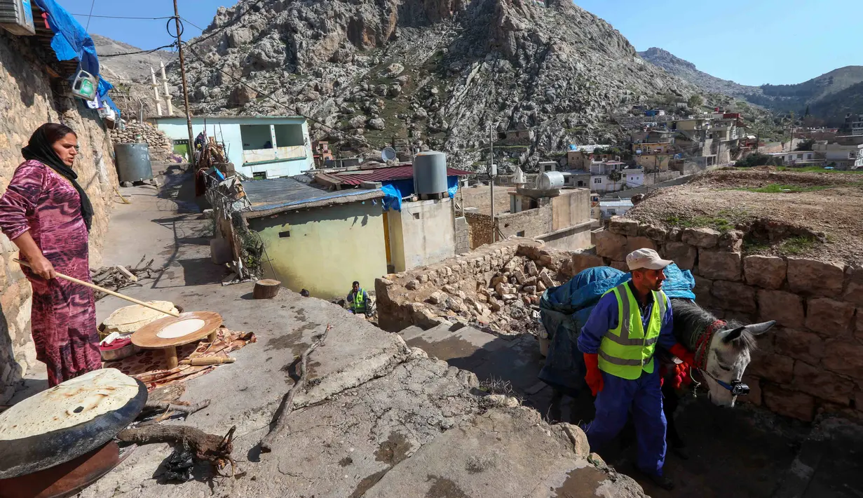 Seorang perempuan membuat roti pipih saat pekerja kota tiba dengan seekor keledai untuk mengumpulkan sampah rumah tangga di kota Akre, sekitar 500 km sebelah utara Baghdad, Irak, 13 Februari 2021. Pemerintah kota Akre menggunakan keledai dan anak kuda untuk mengumpulkan sampah. (SAFIN HAMED/AFP)