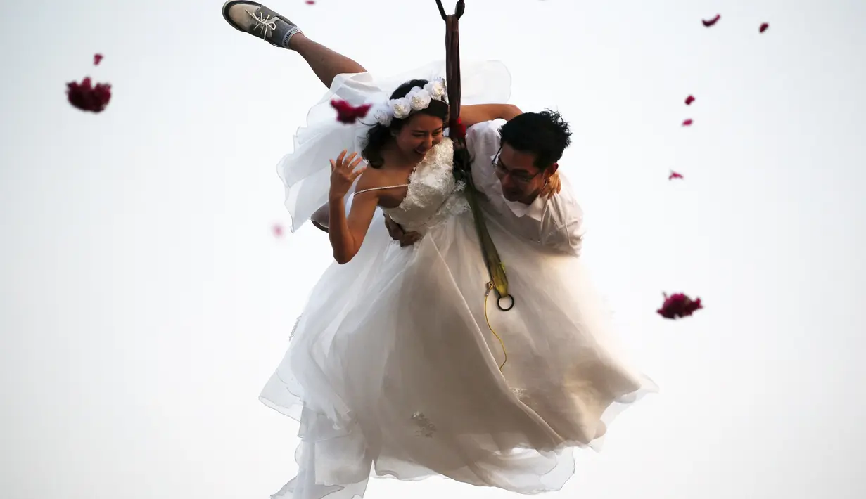 Sepasang pengantin bergelantungan pada sebuah tali saat upacara pernikahan di provinsi Ratchaburi, Thailand, Sabtu (13/2). Upacara pernikahan tersebut diikuti oleh empat pasang pengantin untuk menyambut Hari Valentine. (REUTERS/ Athit Perawongmetha)