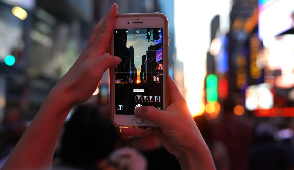 Seorang wanita mengambil gambar fenomena Manhattanhenge, dimana matahari terbenam sejajar tepat dengan jalan, di Times Square, New York City, Kamis (12/7). Manhattanhenge dimana saat matahari terbenam sejajar dengan jalan. (AFP/TIMOTHY A. CLARY)