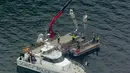 Petugas menggunakan derek dalam operasi pengangkatan bagian pesawat amfibi dari Sungai Hawkesbury, Sydney, Kamis (4/1). Bangkai kapal diangkat ke sebuah tongkang dan ditutupi dengan terpal karena sifat operasi yang sensitif (Mick Tsikas/AAP Images via AP)