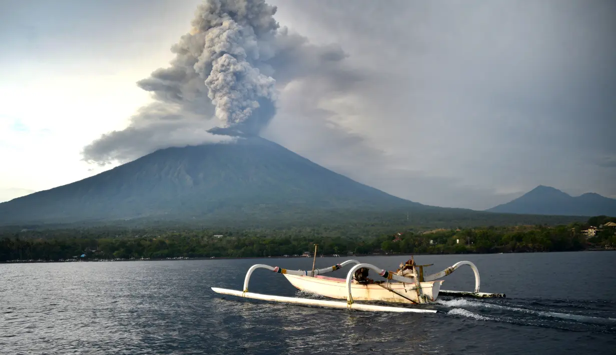 Seorang nelayan berada di atas perahu melihat Gunung Agung yang mengeluarkan asap tebal di Kabupaten Karangasem, Bali (28/11). (AFP Photo/Sonny Tumbelaka)