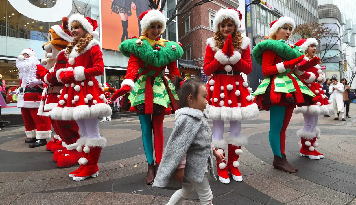 Seorang anak berjalan di depan sejumlah wanita yang mengenakan kostum Santa Claus selama acara mempromosikan musim Natal di sebuah distrik perbelanjaan di Seoul (13/11). (AFP Photo/Jung Yeon-Je)