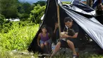 Seorang ayah memberi susu botol jus jeruk kepada putrinya yang masih bayi di tepi Sungai Huixtla, negara bagian Chiapas, Meksiko, Rabu (8/5/2022). Keluarga itu adalah rombongan dari kelompok migran, banyak dari Amerika Tengah dan Venezuela, yang meninggalkan Tapachula. (AP Photo/Marco Ugarte)