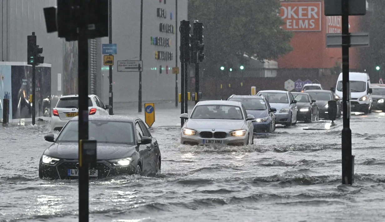 Mobil melintasi jalan yang banjir saat hujan lebat di distrik The Nine Elms London (25/7/2021). Banjir parah terjadi di Ibu Kota Inggris London yang menyebabkan lumpuhnya sejumlah area di kota tersebut. (AFP/Justin Tallis)