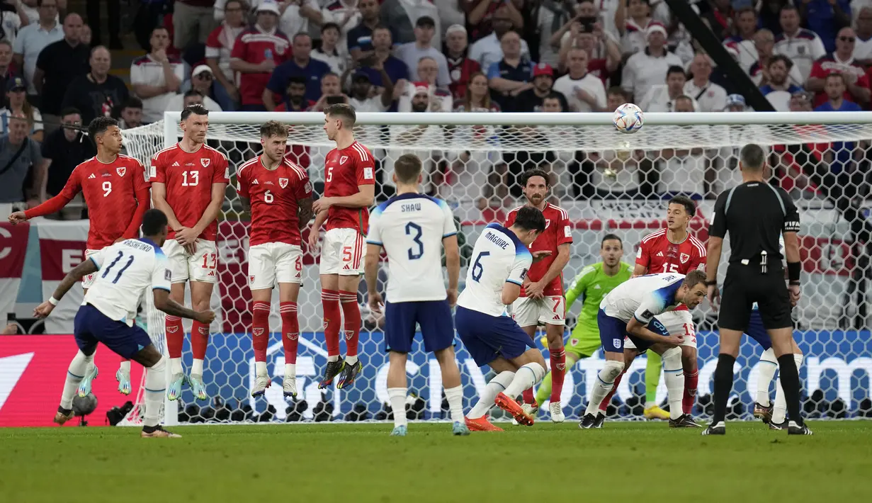 <p>Pemain Inggris, Marcus Rashford (kiri) mencetak gol pertama timnya ke gawang Wales melalui tendangan bebas saat matchday ketiga Grup B Piala Dunia 2022 di Ahmad Bin Ali Stadium, Rabu (30/11/2022). (AP/Thanassis Stavrakis)</p>