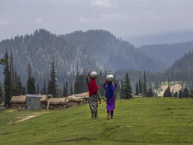 Gadis-gadis penggembala Kashmir berjalan pulang setelah mengambil air dari mata air terdekat di Tosamaidan, barat daya Srinagar, Kashmir yang dikuasai India, Senin (21/6/2021).  Padang rumput Tosamaidan ini dulunya merupakan tempat tembak artileri tentara India. (AP Photo/Dar Yasin)