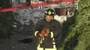 Petugas pemadam kebakaran berjalan keluar dengan anak anjing setelah serangkaian ledakan di Puebla, Meksiko, Minggu (31/10/2021). Penyadapan ilegal pada saluran gas diduga menjadi penyebab ledakan yang menewaskan sedikitnya satu orang dan melukai lebih dari selusin. (AP Photo/Pablo Spencer)