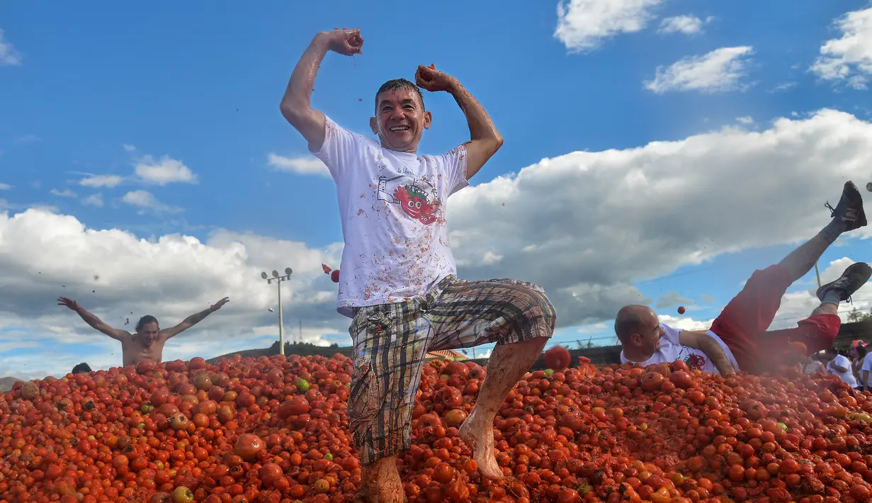Peserta berdiri di atas gundukan tomat saat Festival Tomatina di Sutamarchan, Boyaca, Kolombia, Minggu (2/6/2019). Perang tomat ini digelar selama tiga hari berturut-turut. (Diana SANCHEZ/AFP)