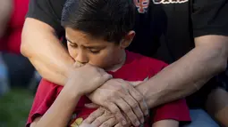 Seorang anak memegang tangan ayahnya saat menghadiri acara berjaga-jaga untuk korban penembakan brutal di festival kuliner Gilroy Garlic di Gilroy, California (29/7/2019). Dalam kejadian tersebut polisi berhasil menembak palaku penyerangan. (AP Photo/Noah Berger)
