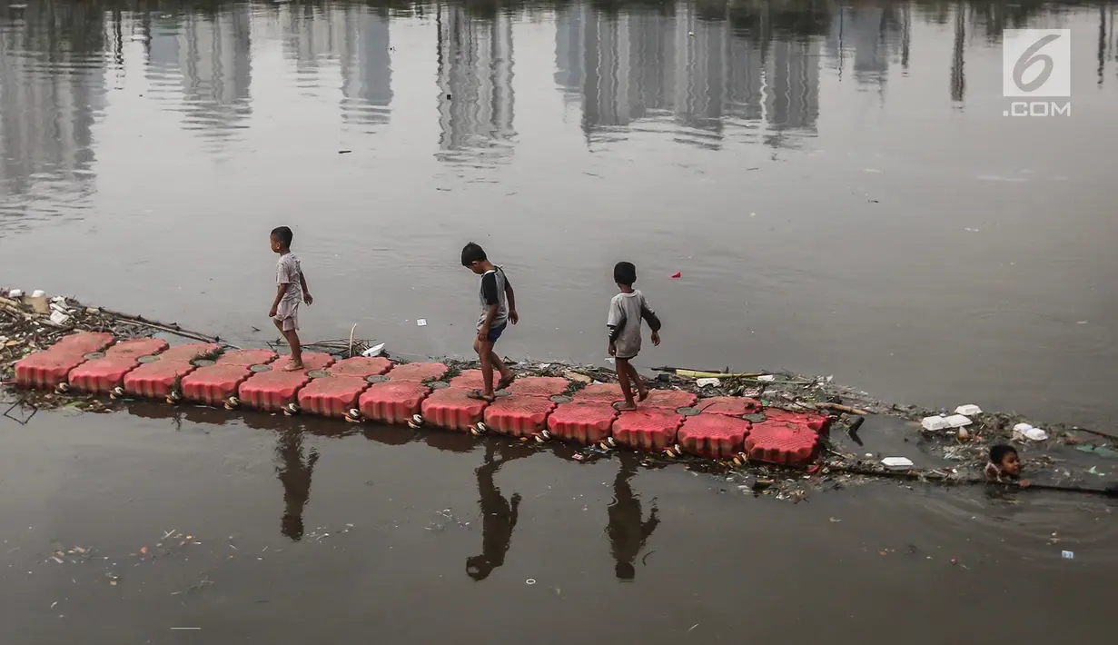 Anak-anak berjalan di atas jembatan penyaring sampah di Sungai Banjir Kanal Barat, Petamburan, Jakarta, Jumat (9/11). Mereka memanfaatkan waktu bermain usai pulang sekolah. (Liputan6.com/Fery Pradolo)
