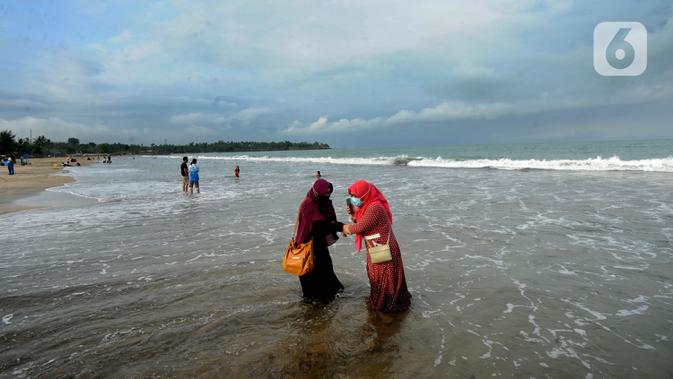 Wisatawan yang mengenakan masker bermain air saat mengunjungi Pantai Anyer di Cilegon, Banten, Minggu (25/10/2020). Akhir pekan dimanfaatkan warga Jakarta dan sekitarnya untuk berwisata dengan tetap menerapkan protokol kesehatan Covid-19. (merdeka.com/Arie Basuki)