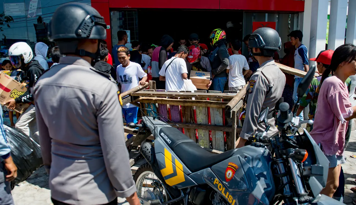 Petugas kepolisian melihat warga menjarah toko swalayan setelah gempa kuat dan tsunami mengguncang Kota Palu di Sulawesi Tengah, Minggu (30/9). Warga terpaksa mengambil karena mereka juga membutuhkan makanan dan air bersih. (AFP PHOTO/BAY ISMOYO)