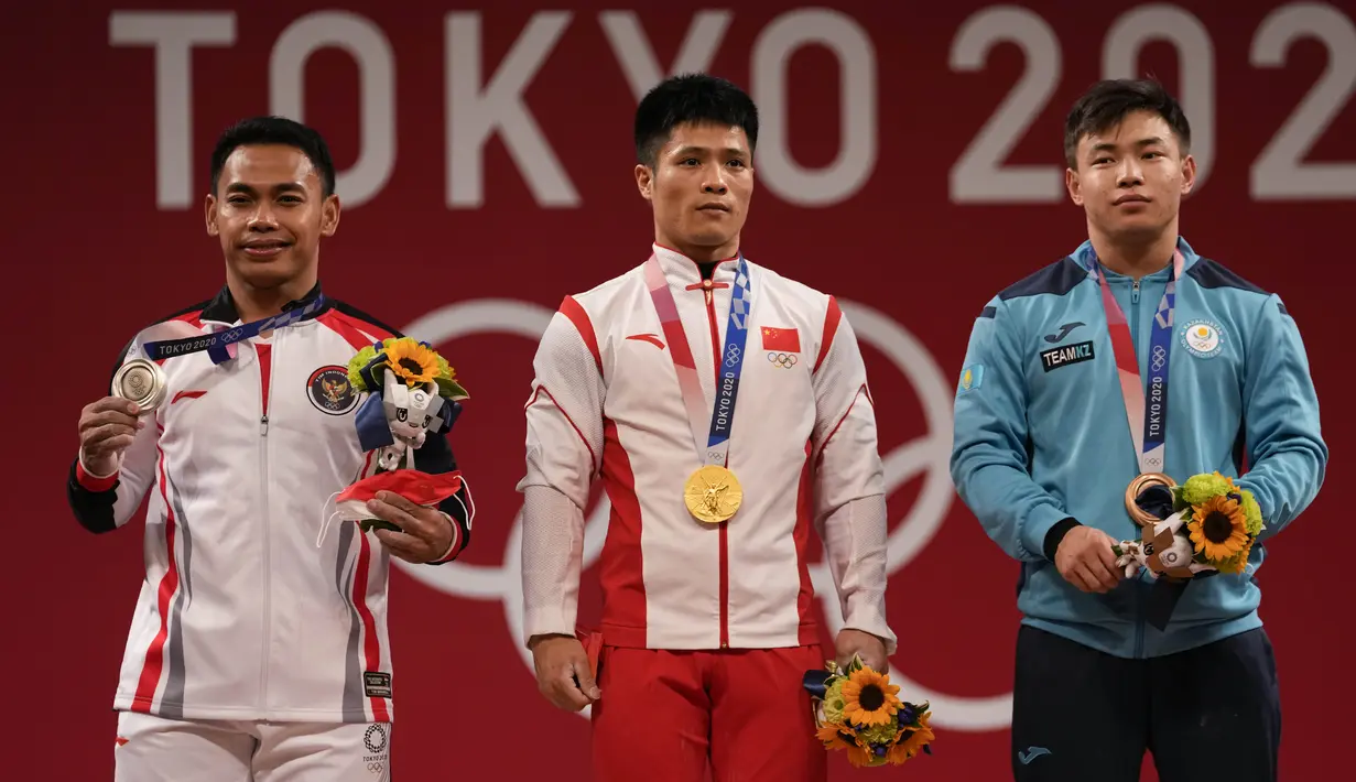 Peraih medali emas Li Fabin dari China (tengah) berdiir bersama peraih medali perak Eko Yuli Irawan dari Indonesia (kiri) dan peraih medali perunggu Igor Son dari Kazakhstan seusai kompetisi kelas 61kg putra cabor angkat besi Olimpiade Tokyo 2020 di Tokyo, Minggu (25/7/2021). (AP Photo/Luca Bruno)