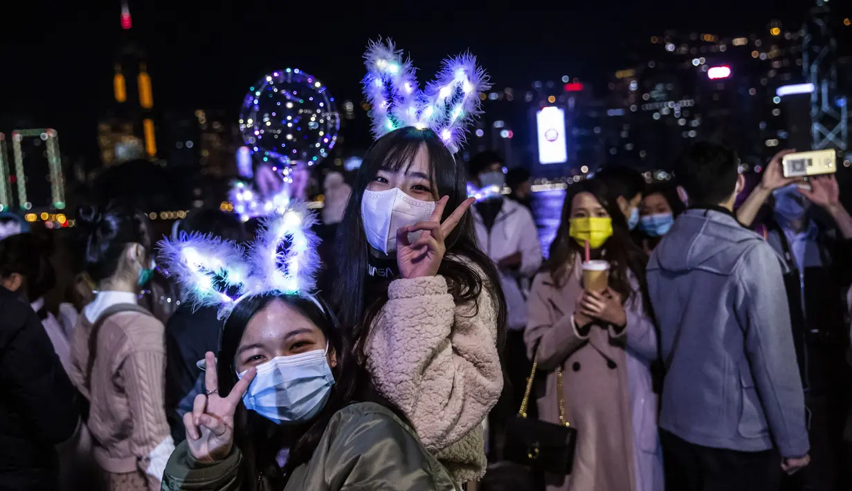Dua wanita berpose di samping tepi perairan Pelabuhan Victoria di Hong Kong (1/1/2020). Meskipun ada pembatasan virus corona COVID-19 dan kembang api Tahun Baru dibatalkan, orang-orang berkumpul untuk merayakan Tahun Baru. (AFP/Isaac Lawrence)