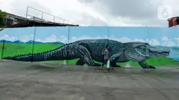 Warga melintasi kreasi mural di sepanjang dinding bantaran Kali Opak, Jakarta Utara, Kamis (6/2/2020). Tembok bangunan saat ini tak hanya menjadi pembatas semata tapi dimanfaatkan untuk menyampaikan pesan-pesan dan harapan dalam bentuk goresan atau tulisan. (merdeka.com/Imam Buhori)