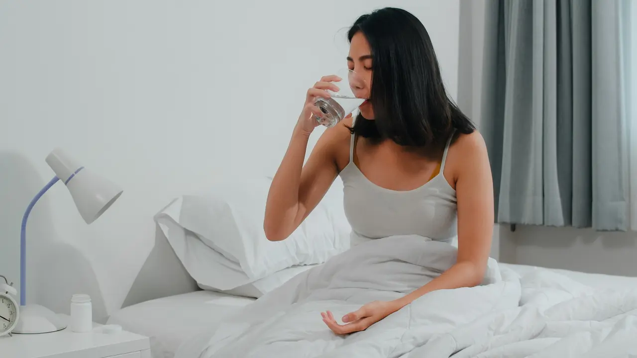 Seorang perempuan yang sedang sakit meminum segelas air putih (Foto Dok: Freepik/tirachardz)