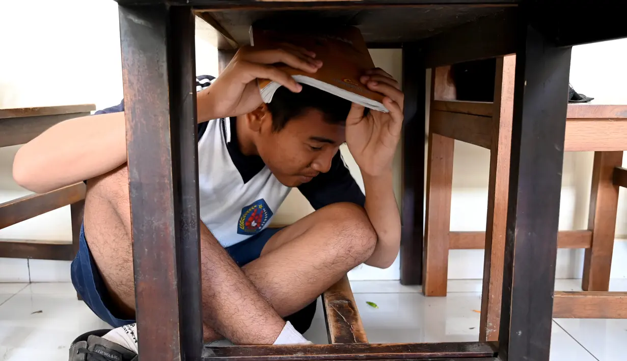 Seorang siswa berlindung di bawah meja saat mengikuti simulasi gempa bumi dan tsunami di Jimbaran, Bali (5/11/2019). Latihan dilakukan untuk memberikan pengajaran kepada siswa agar mengantisipasi bahaya bencana gempa bumi dan tsunami yang bisa datang sewaktu-waktu. (AFP Photo/Sonny Tumbelaka)