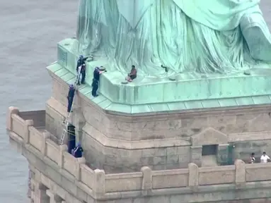 Petugas kepolisian membujuk seorang wanita yang memanjat Patung Liberty di New York, Rabu (4/7). Aksi wanita bernama Therese Okoumou ini memprotes kebijakan imigrasi pemerintah Presiden Donald Trump yang memisahkan keluarga migran. (AFP/PIX11 News/HO)