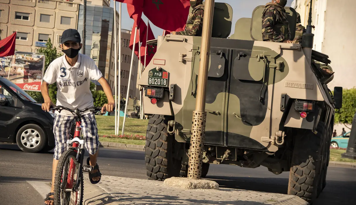 Seorang anak mengendarai sepeda saat tentara Maroko berpatroli di tengah wabah baru virus corona baru di kota Tangiers (11/8/2020). Tentara dikerahkan untuk meredam Lonjakan kasus Covid-19 di negara tersebut. (AFP/Fadel Senna)