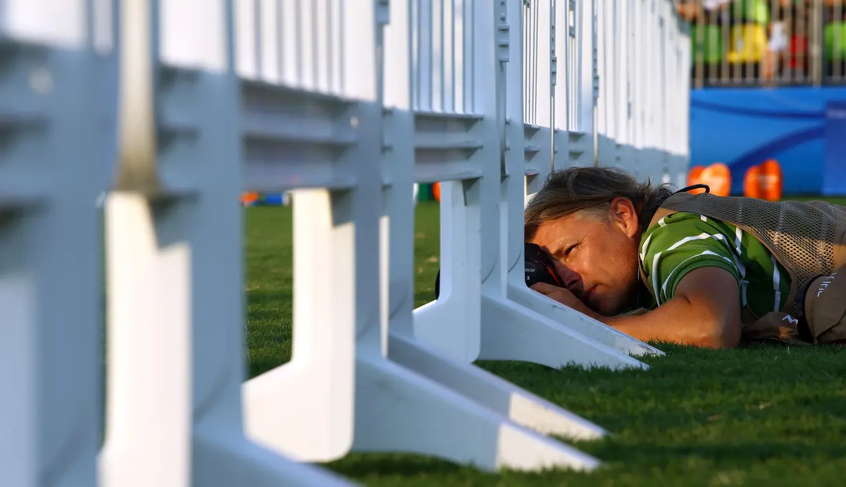 Seorang fotografer tengkurap di sebuah rumput saat mengambil momen terbaik balapan kuda wanita pada Olimpiade Rio 2016 di Deodoro Stadium, Rio de Janeiro, Brasil, (15/8). (REUTERS / Jeremy Lee)