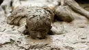 Seorang anak berendam dalam lumpur saat berpartisipasi dalam perayaan Mud Day atau Hari Lumpur di Wayne County di Nankin Mills Park, Westland, Michigan, AS (11/7). (AFP Photo/Jeff Kowalsky)