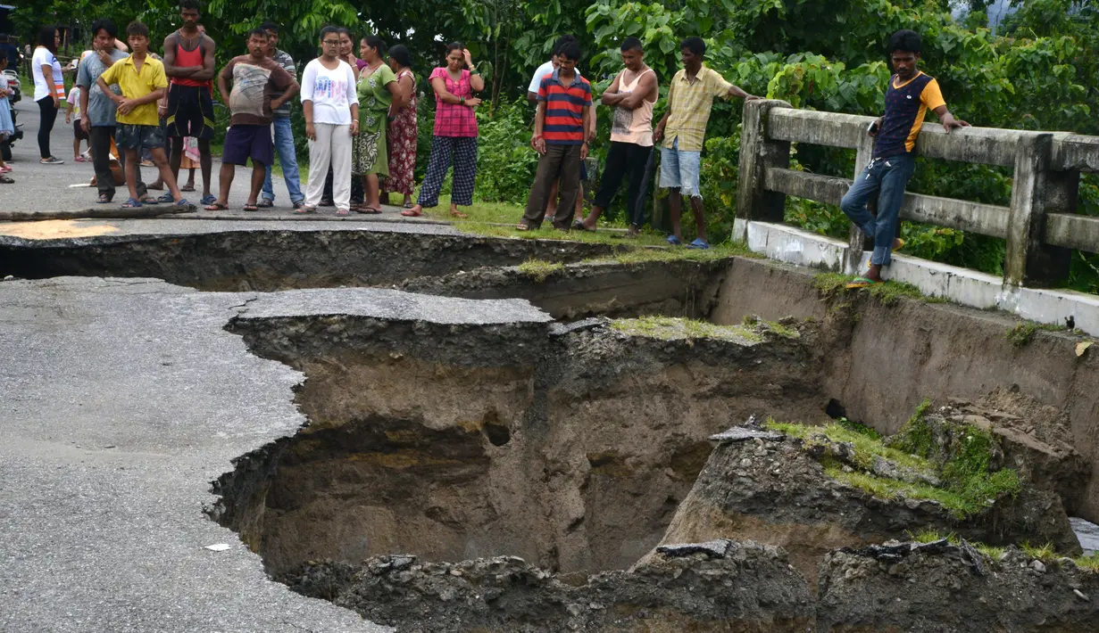 Sejumlah warga India mengamati sebuah jembatan yang hancur akibat hujan deras di Desa Toribari, pinggiran Siliguri, Kamis (21/7). Hujan deras yang terus menerus turun di India dalam 48 jam terakhir menyebabkan banjir dan tanah longsor (DIPTENDU Dutta/AFP)