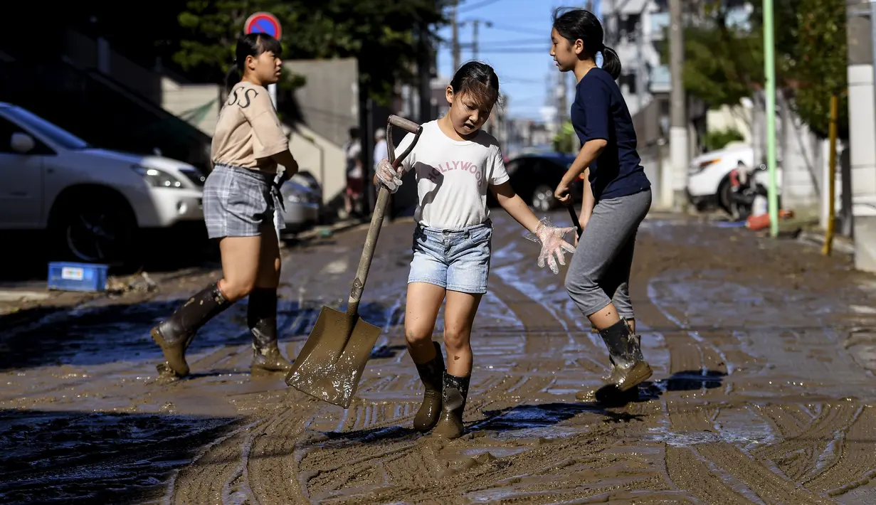 Anak-anak membersihkan lumpur dari jalan setelah banjir surut di Kawasaki, Minggu (13/10/2019). Topan dahsyat Hagibis yang menerjang sejumlah wilayah di Jepang menyebabkan banjir di beberapa lokasi. (Photo by WILLIAM WEST / AFP)