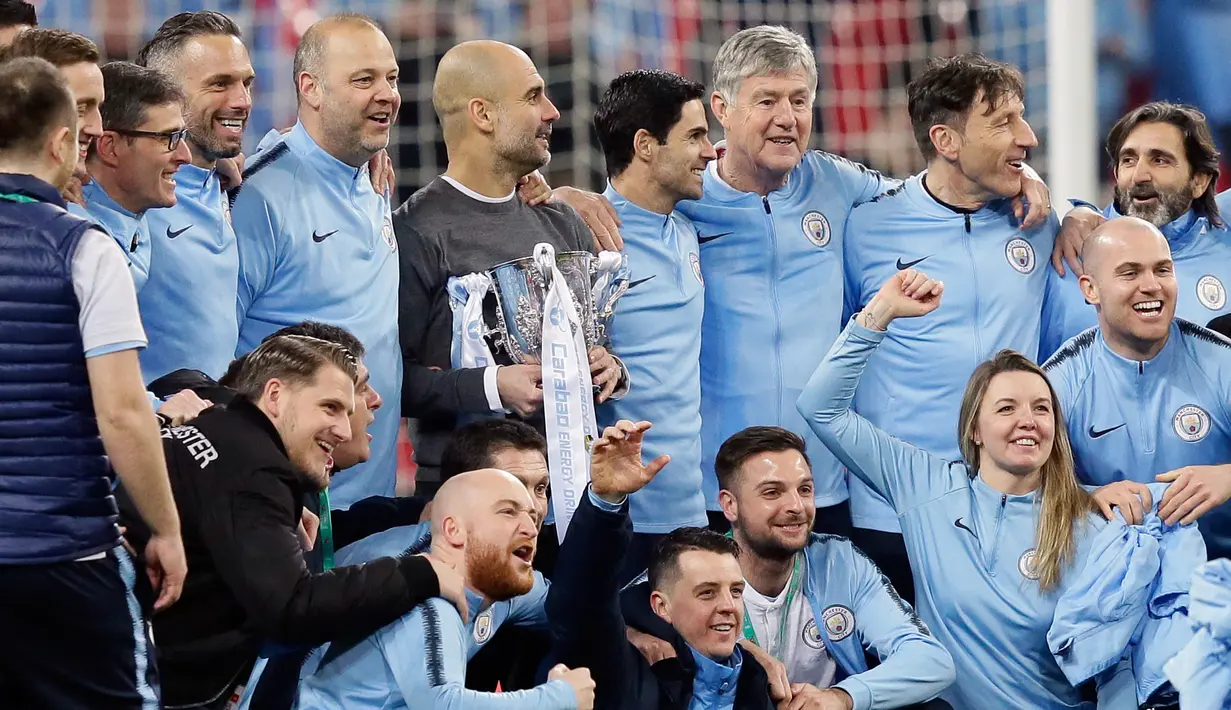 Manajer Manchester City Josep Guardiola (tengah) memegang trofi dan berfoto bersama para pemain serta staf setelah memenangkan pertandingan final Piala Liga Inggris melawan Chelsea di stadion Wembley, London, Minggu (24/2). (AP Tim Ireland)