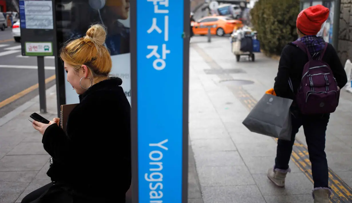 Seorang wanita bermain ponsel saat menunggu di halte bus di Seoul, Korea Selatan (19/2). (AFP Photo/David Gannon)