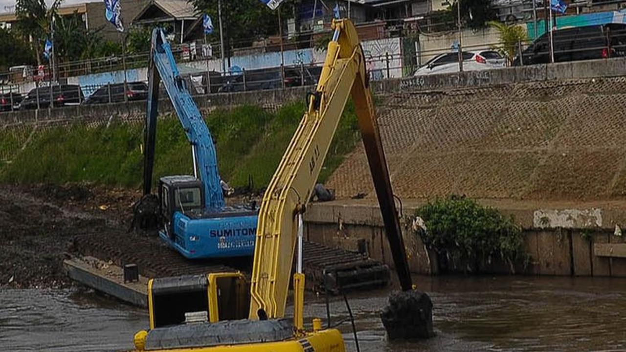 Pekerja menggunakan ekskavator untuk mengeruk material lumpur yang mengendap di Kali Ciliwung, Jakarta, Selasa (16/1/2023).