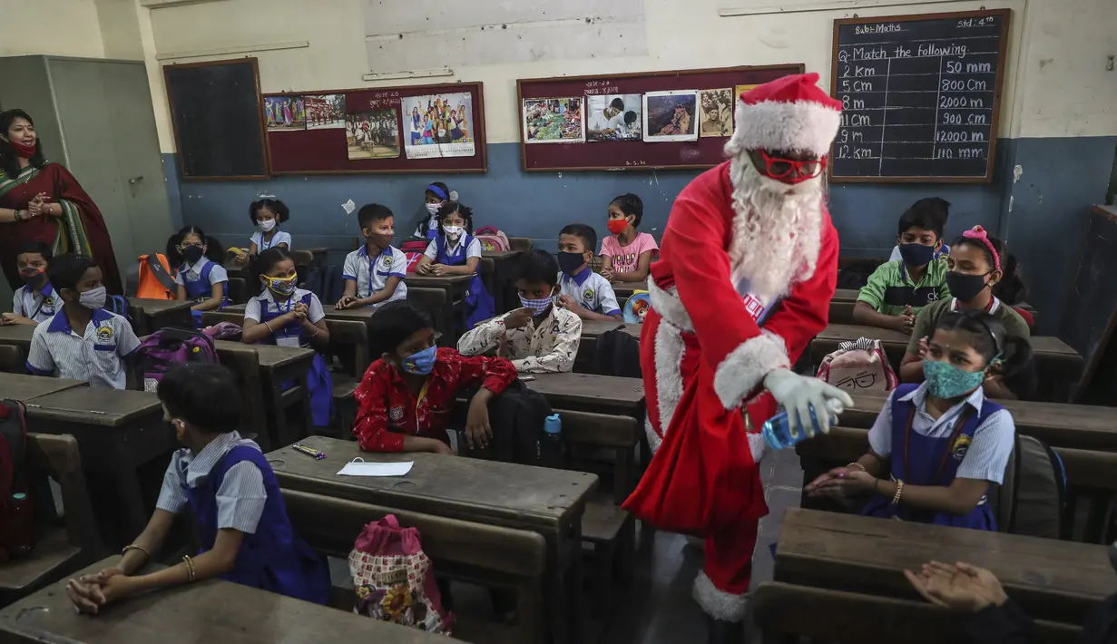 Seorang pria berpakaian Sinterklas memberikan sanitizer kepada siswa saat bersiap memulai kelas di sebuah sekolah di Mumbai, India, Rabu (15/12/2021). Setelah ditutup selama hampir 20 bulan karena pandemi virus corona, sekolah di Mumbai dibuka kembali untuk kelas 1 sampai 7. (AP Photo/Rafiq Maqbool)