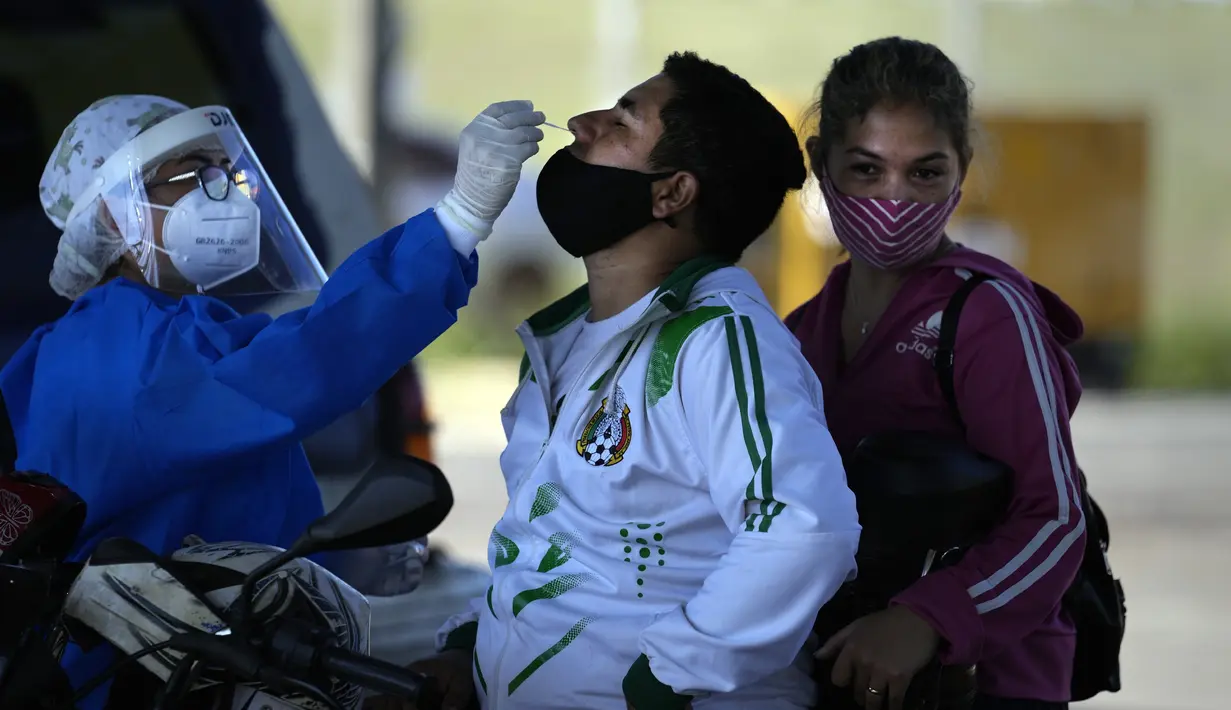 Seorang petugas kesehatan mengambil sampel usap hidung dari seorang pria untuk tes COVID secara gratis di tempat pengujian drive-thru di arena pacuan kuda di Capiata, Paraguay, Selasa (11/1/2022).  (AP Photo/Jorge Saenz)