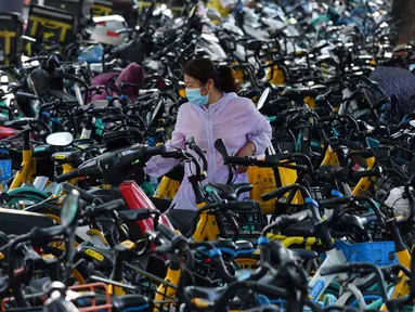 Seorang wanita berjalan melintasi sepeda-sepeda yang diparkir di atas trotoar di Beijing, China (21/7/2020). Seperti diketahui Beijing telah menerapkan bike sharing yang sudah tersedia di trotoar-trotoar Kota Beijing. (AFP Photo/Greg Baker)