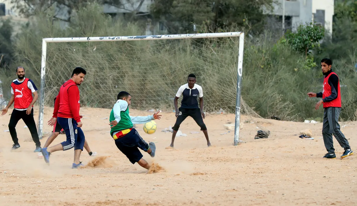 Seorang pemain menembak bola saat bermain di lapangan tanah sebelum buka puasa selama bulan Ramadhan, di ibu kota Libya, Tripoli (24/4/2021). (AFP/Mahmud Turkia)
