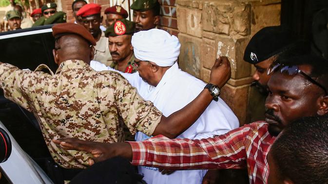 Mantan Presiden Sudan, Omar al-Bashir, dikawal setelah menghadap jaksa untuk pembacaan dakwaan terkait kasus korupsi di ibu kota Khartoum, Minggu (16/6/2019). Ini merupakan penampilan pertamanya di hadapan publik sejak kudeta penggulingan dirinya pada April lalu. (Yasuyoshi CHIBA/AFP)